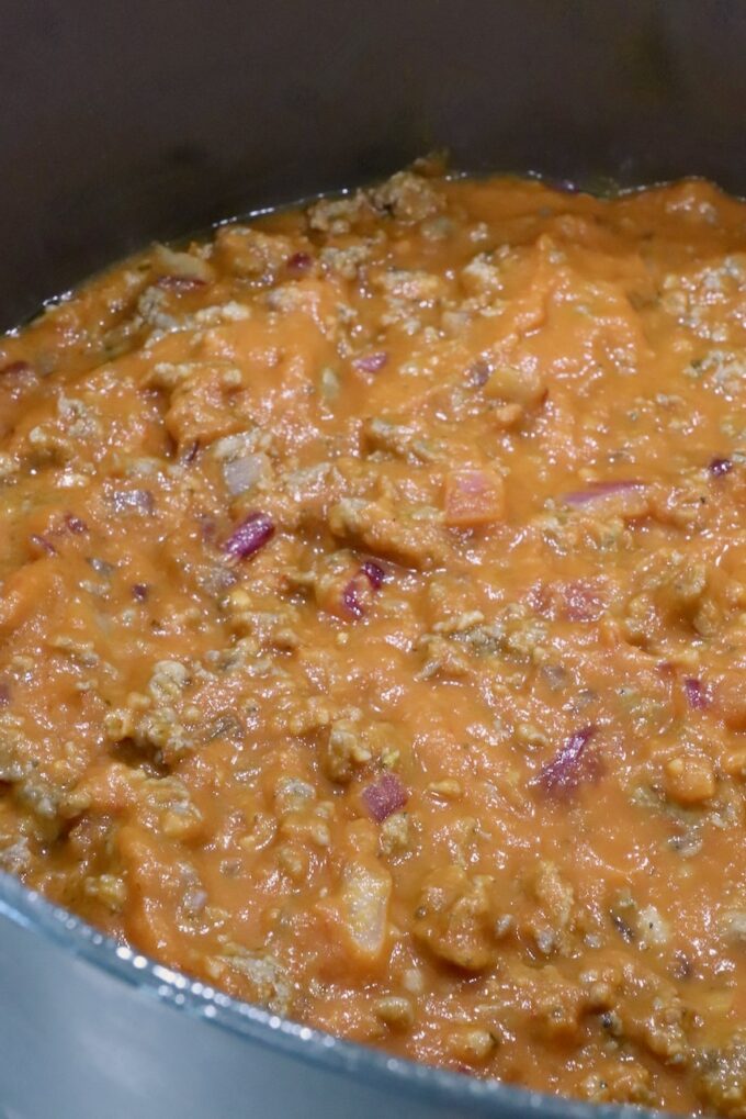 Close-up of a butternut squash meat sauce in a pot, featuring a rich orange sauce with chunks of meat and onions