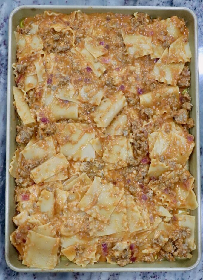 uncooked lasagna on a sheet pan with wavy pasta tossed with ground meat, sauce, and cheese