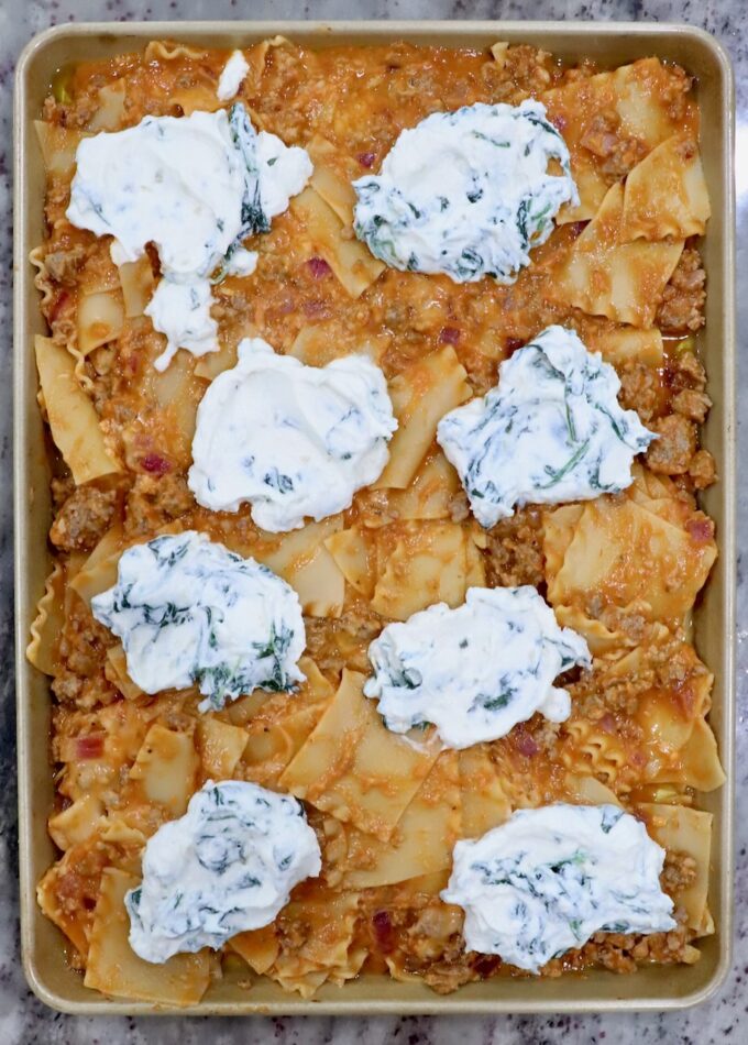 uncooked lasagna on a sheet pan topped with large dollops of spinach ricotta cheese