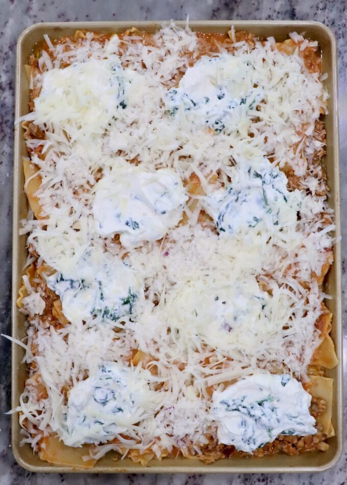 uncooked lasagna on a sheet pan topped with ricotta cheese and shredded mozzarella cheese