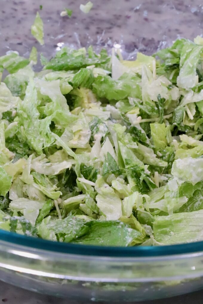 Chopped lettuce with grated cheese in a glass bowl on a speckled countertop. 