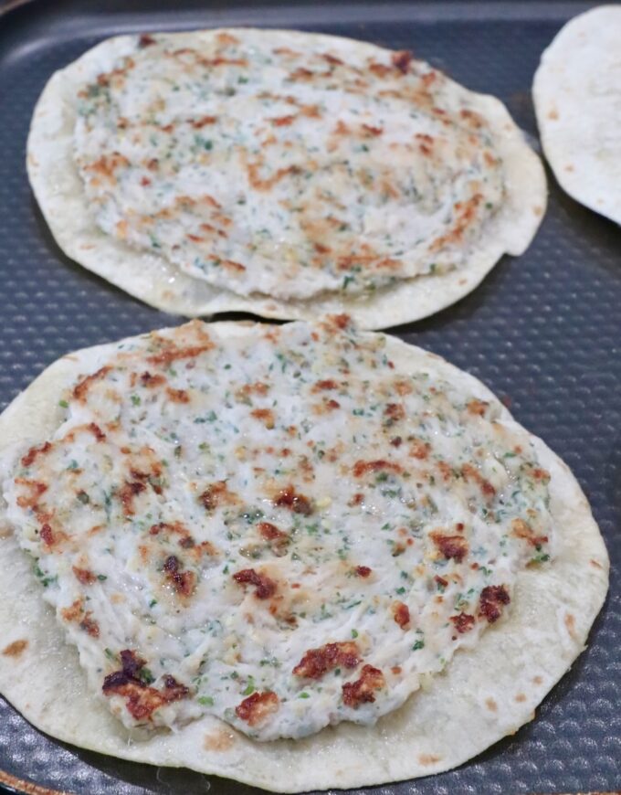Two tortillas topped with an herb-speckled chicken mixture sit on a textured, dark griddle pan