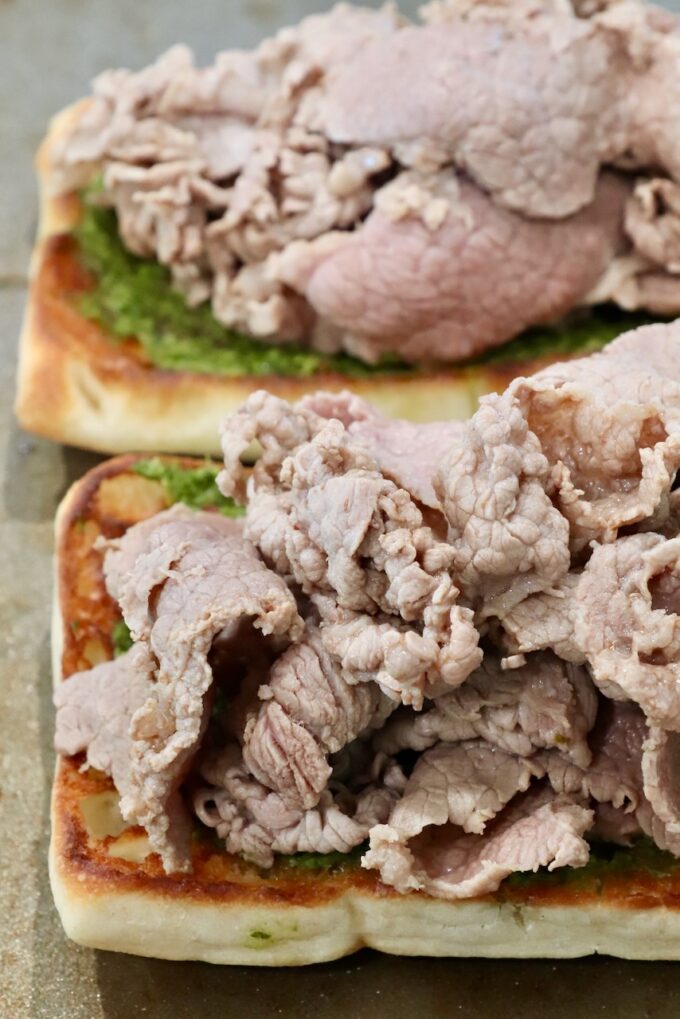 Close-up of two open-faced sandwiches with thinly sliced roast beef atop toasted bread with green chimichurri sauce