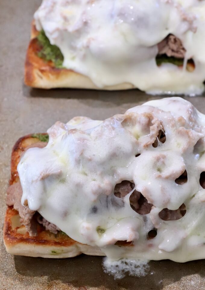 Toasted bread slices topped with roasted beef, chimichurri sauce, and melted cheese. 