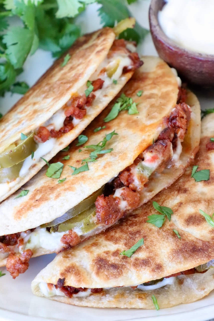 Three crispy tacos filled with chorizo, cheese, and jalapeños are garnished with cilantro. A small bowl of white queso sits beside them.