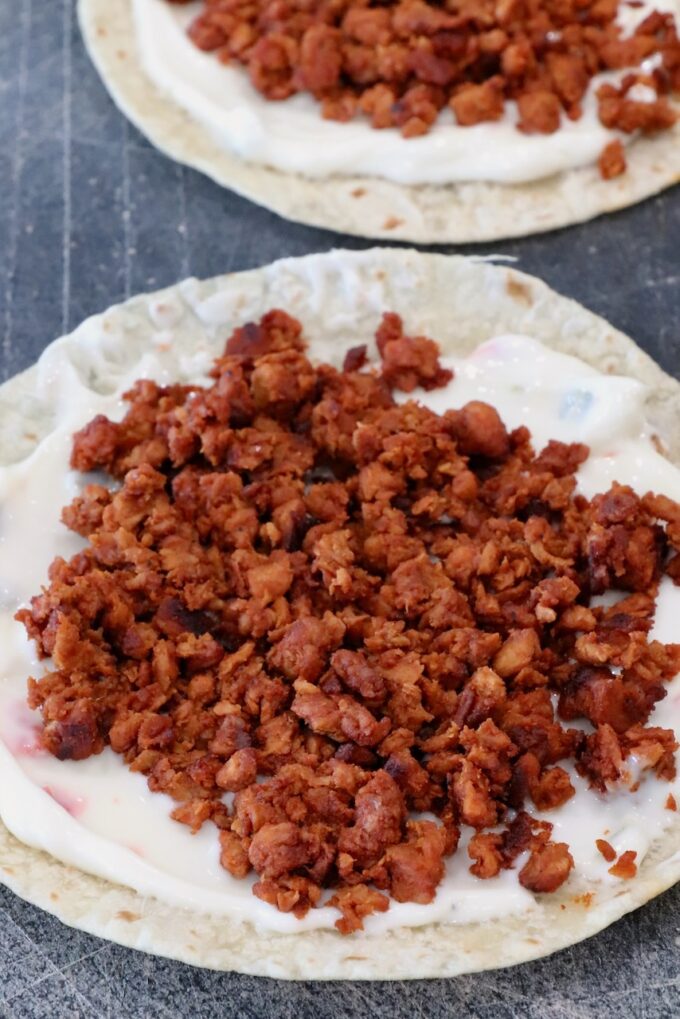 cooked, crumbled chorizo on top of queso on a tortilla