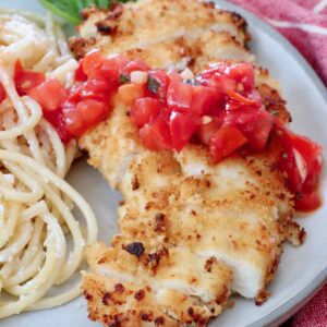 crispy chicken sliced on a plate topped with tomato bruschetta with creamy pasta noodles on the side