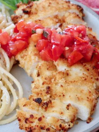 crispy chicken sliced on a plate topped with tomato bruschetta with creamy pasta noodles on the side