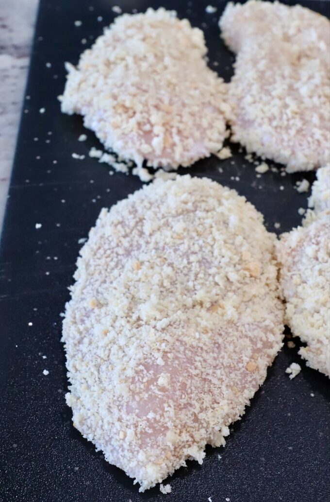 raw chicken breasts coated in breadcrumbs on a cutting board