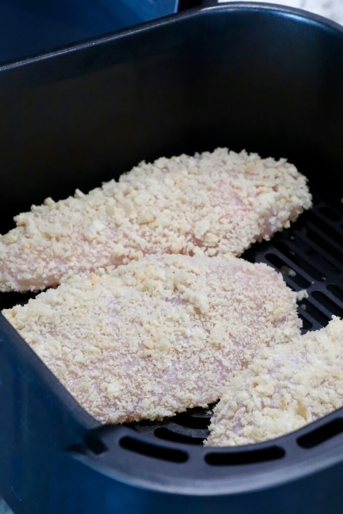 raw chicken breasts coated in breadcrumbs in an air fryer basket