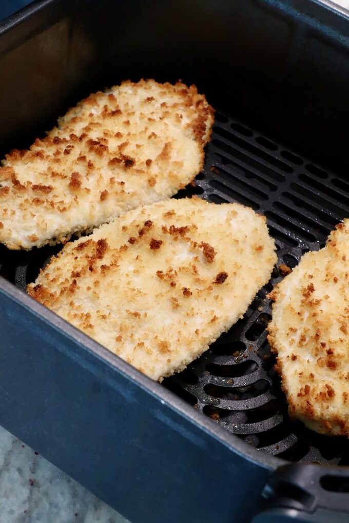 cooked crispy chicken breasts coated in breadcrumbs in an air fryer basket