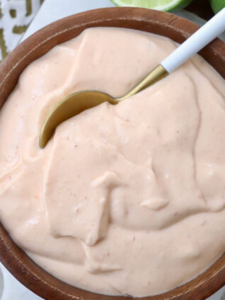 A wooden bowl filled with creamy, light orange sauce. A spoon dips into the smooth mixture.