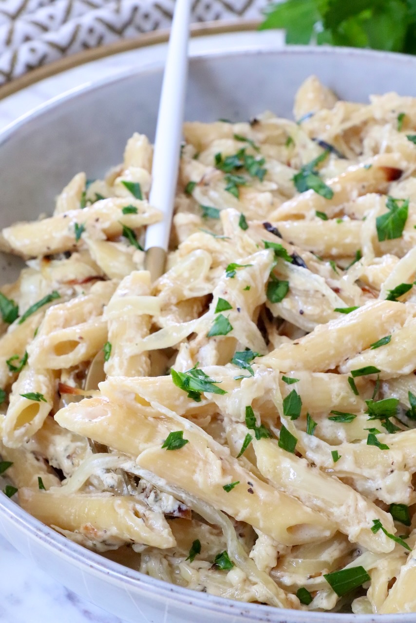 Creamy penne pasta topped with fresh parsley in a white bowl, accompanied by a white and gold spoon. 