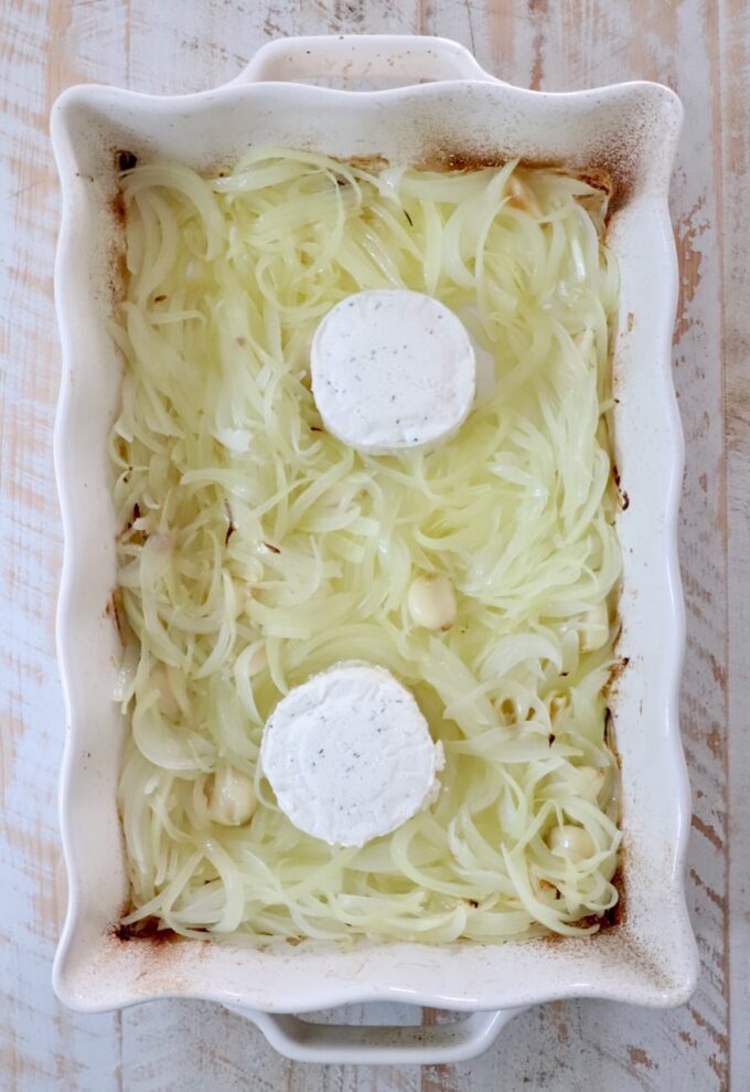 sliced caramelized onions in a white casserole dish with two rounds of boursin cheese