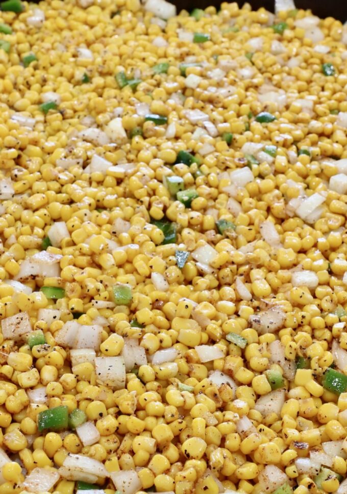 seasoned kernels of corn mixed with diced onions, jalapenos and garlic cloves on a baking sheet