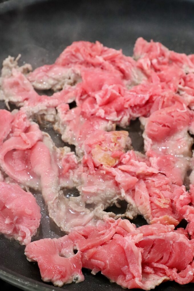 partially cooked thinly sliced steak in a skillet