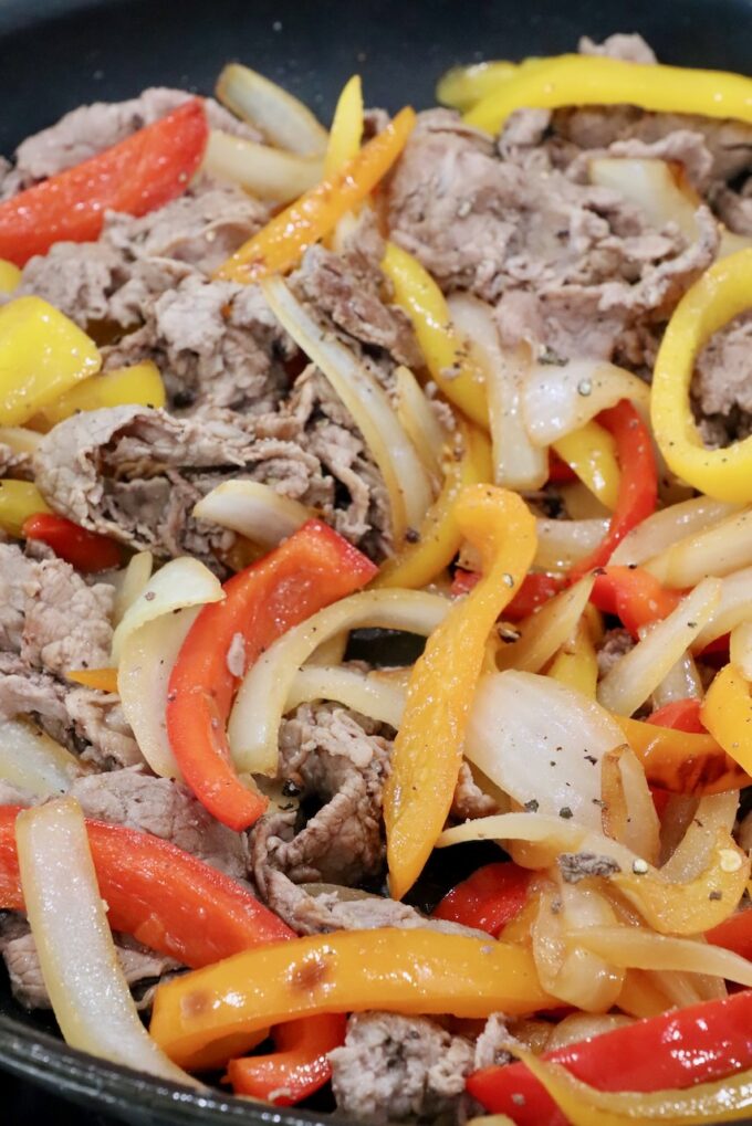 cooked steak, bell peppers, and onions in a skillet