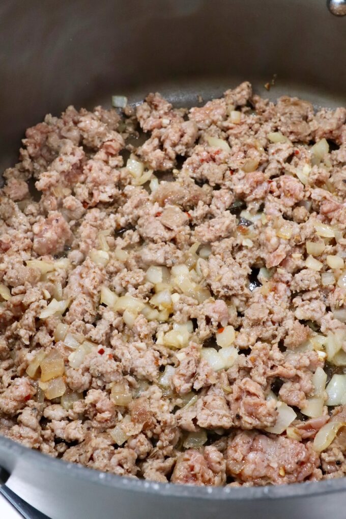Ground meat is being browned with onions in a large skillet. 