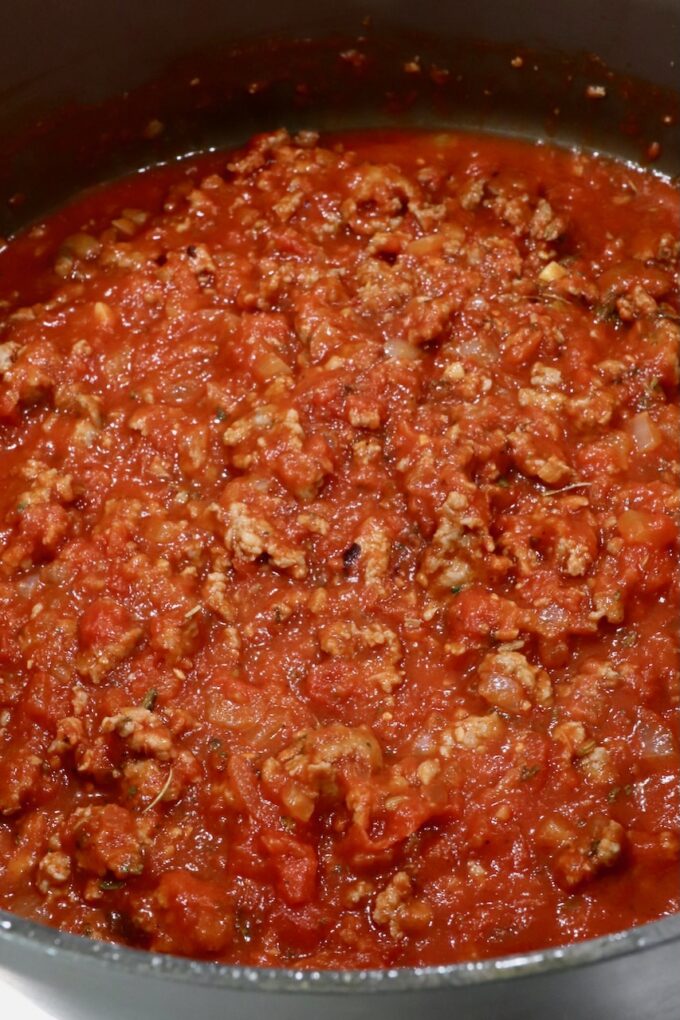 Close-up of a simmering pot of rich red tomato meat sauce, featuring ground meat and diced tomatoes