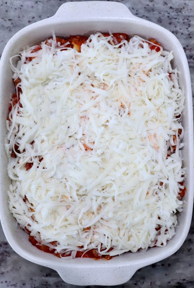 A casserole dish filled with baked ravioli, topped generously with shredded cheese. The cheese covers a layer of tomato sauce.