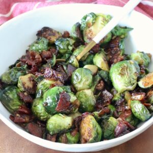 Caramelized Brussels sprouts with crispy bacon pieces in a white bowl with a serving spoon.