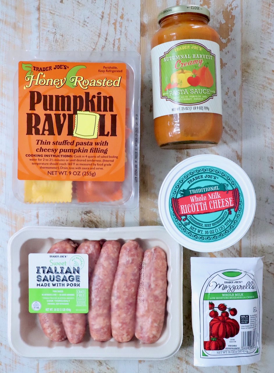 Trader Joe's ingredients on a wooden surface: Honey Roasted Pumpkin Ravioli, Autumnal Pasta Sauce, Sweet Italian Sausage, Ricotta Cheese, Mozzarella.