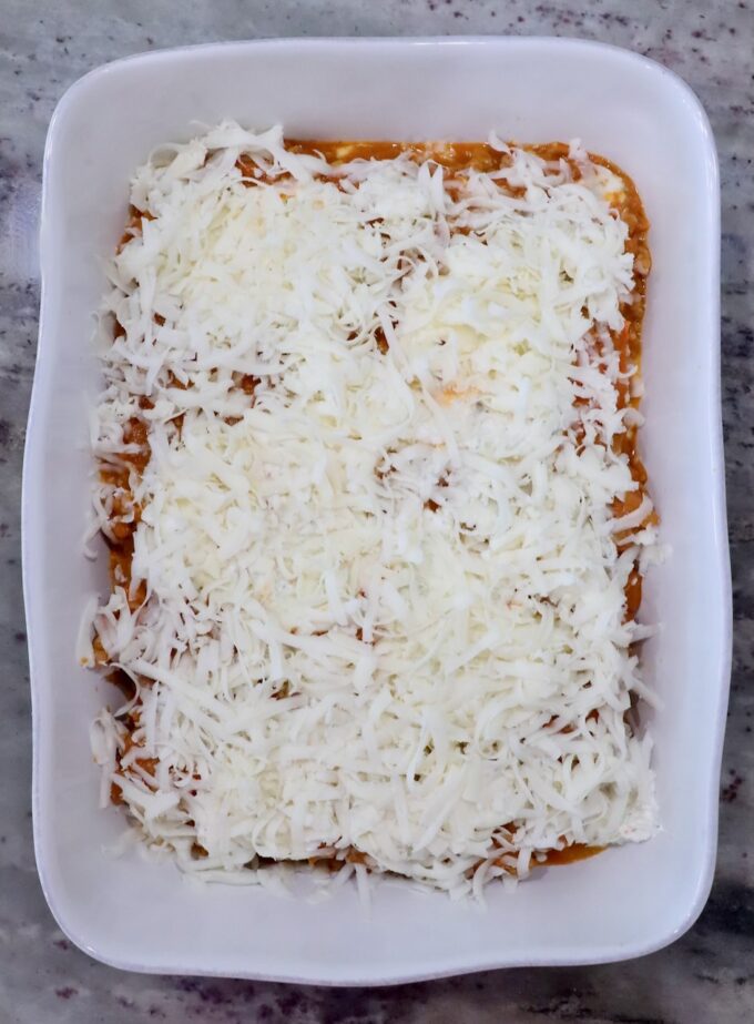White rectangular baking dish filled with layered pumpkin ravioli, topped with shredded mozzarella cheese. 
