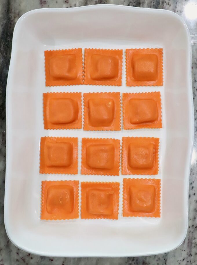 Twelve pumpkin ravioli arranged neatly in a rectangular white dish on a marble countertop