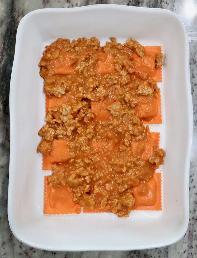 pumpkin ravioli in a baking dish, topped with butternut squash meat sauce