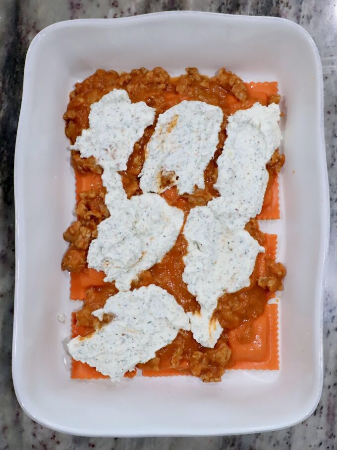 pumpkin ravioli in a baking dish, topped with butternut squash meat sauce and seasoned ricotta cheese