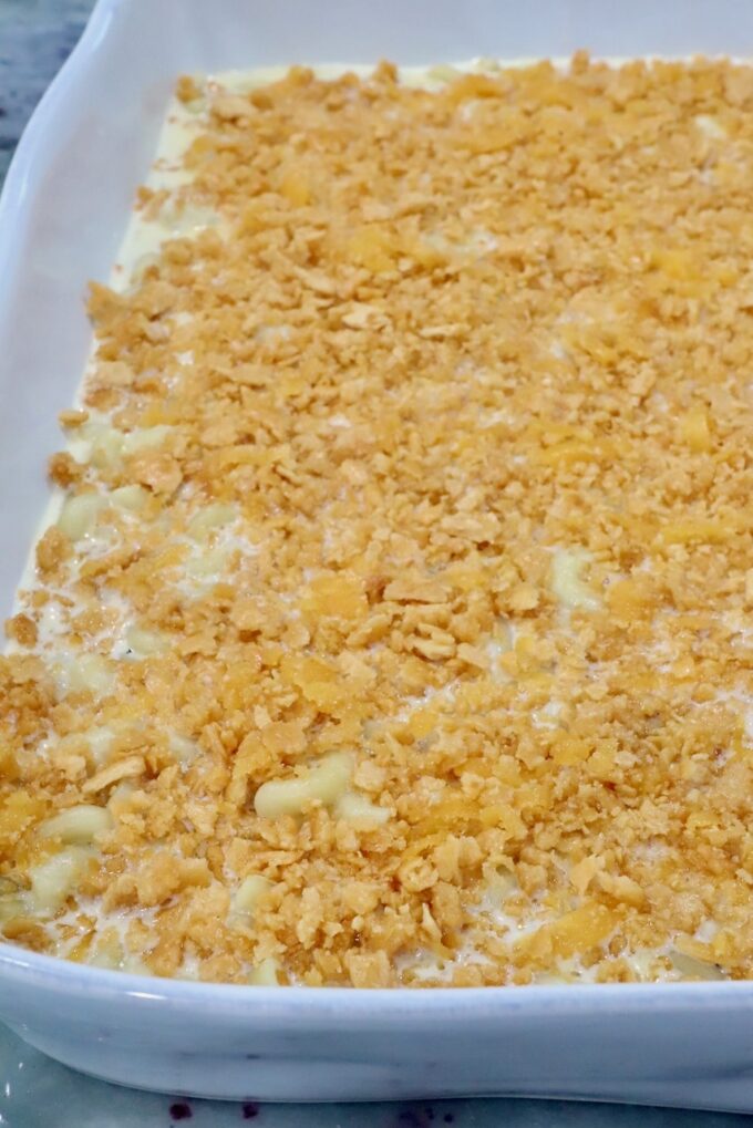 A white baking dish filled with creamy macaroni and cheese is topped with a golden, crumbly crus