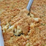 Close-up of creamy macaroni and cheese topped with golden, crispy Cheez-It cracker topping. A serving spoon is lifting up a portion, revealing gooey cheese beneath.