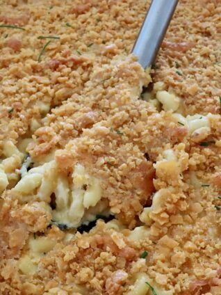 Close-up of creamy macaroni and cheese topped with golden, crispy Cheez-It cracker topping. A serving spoon is lifting up a portion, revealing gooey cheese beneath.