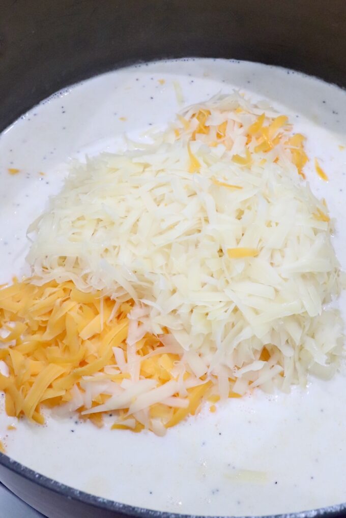 Shredded cheese melting into a creamy white sauce in a pot.