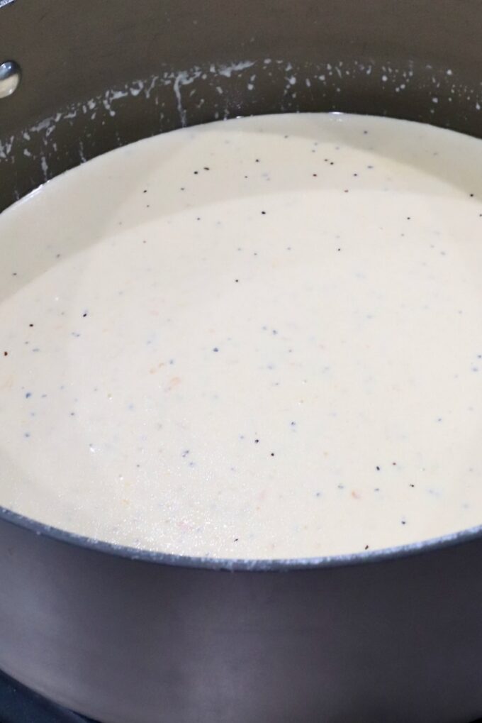 A pot filled with creamy white sauce speckled with small black and red flakes.