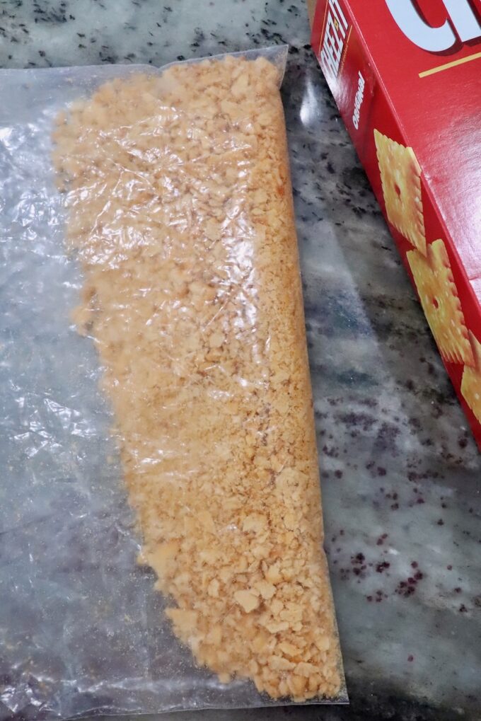 Cracker crumbs in a clear plastic bag on a speckled countertop beside a red cracker box