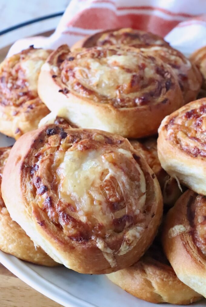 Close-up of golden-brown cheese and onion buns on a white plate. The swirled bread shows a crispy texture.