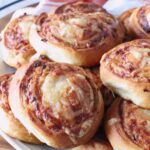 Close-up of golden-brown french onion rolls on a white plate. The swirled bread shows a crispy texture.