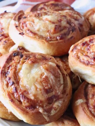 Close-up of golden-brown french onion rolls on a white plate. The swirled bread shows a crispy texture.