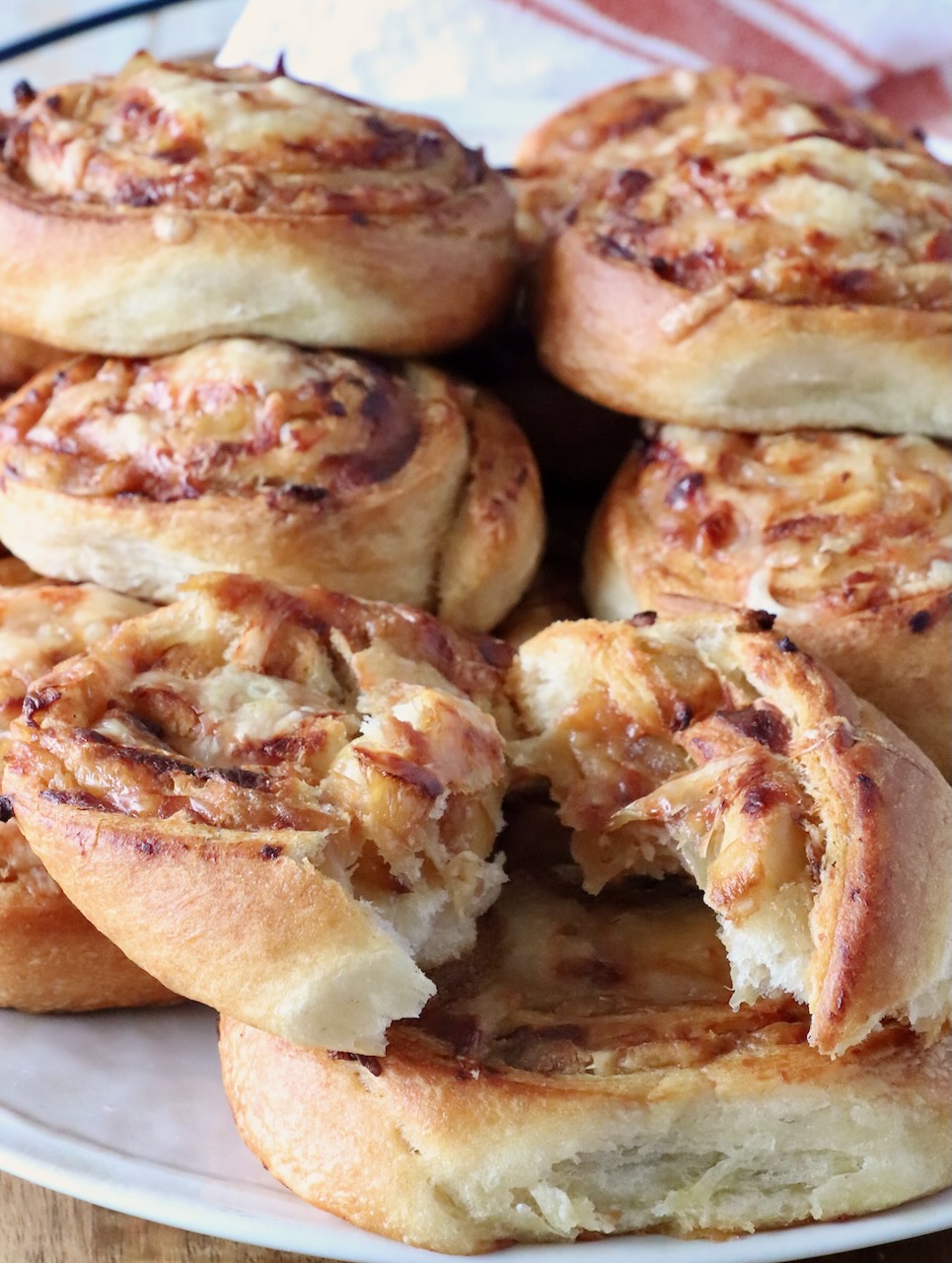 A plate of golden-brown, onion and cheese-filled pastries stacked up on a plate. The pastries have a flaky texture, with one torn open, revealing gooey, melted cheese inside.