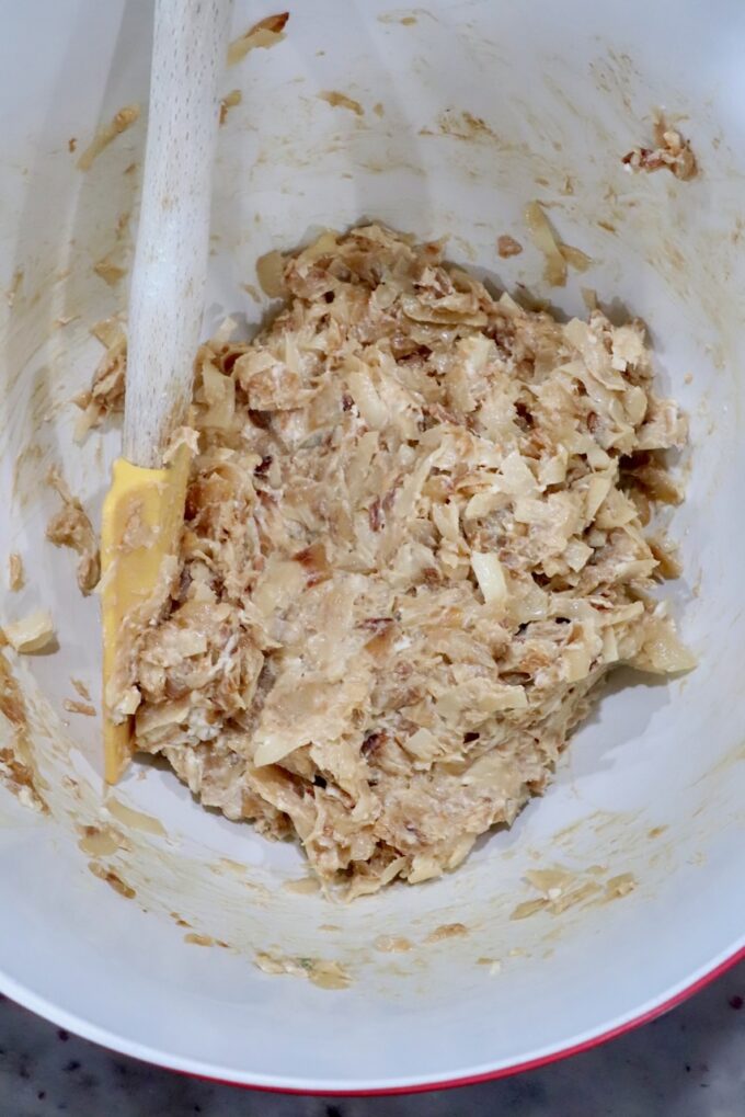 A mixing bowl contains a creamy caramelized onion mixture with a yellow spatula in the bowl.