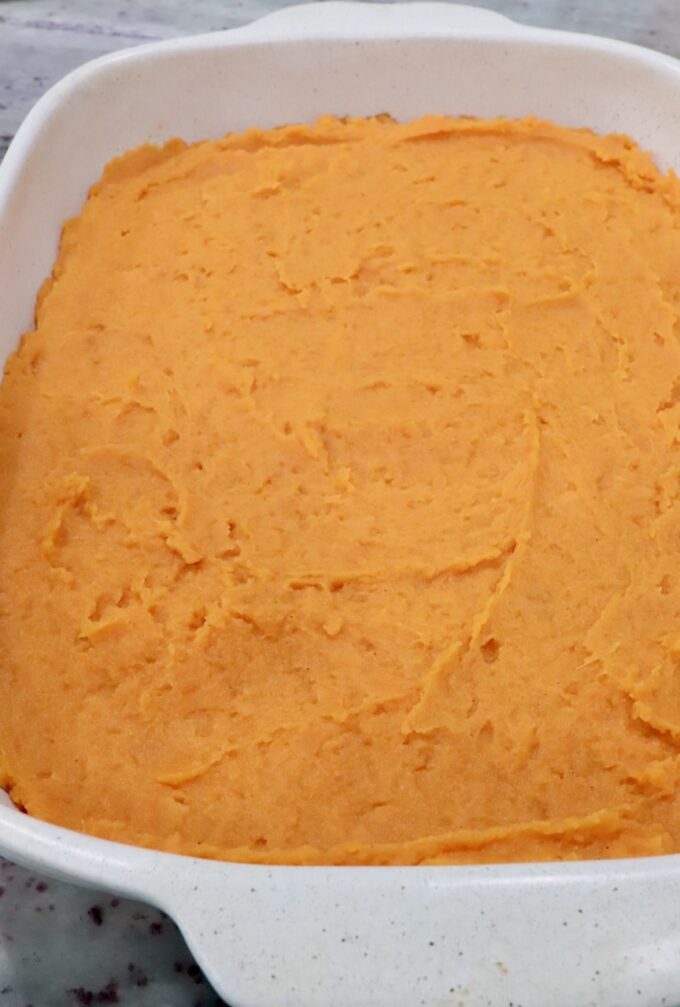 Creamy orange mashed potatoes in a white square dish, spread evenly.