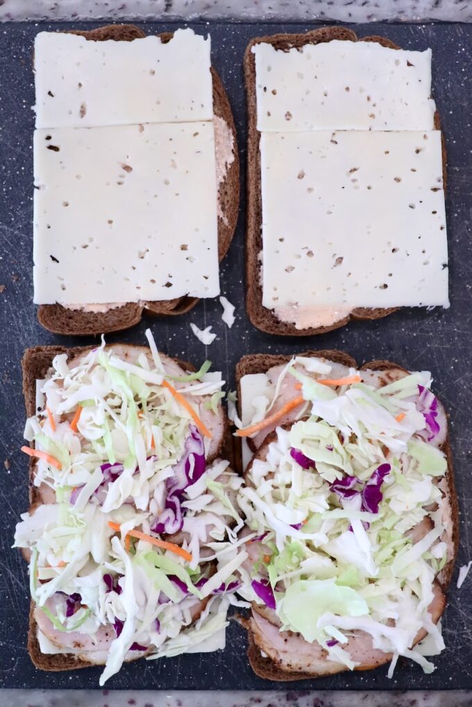 Open rye bread sandwiches: two with sliced cheese, two with coleslaw and meat, on a dark surface.