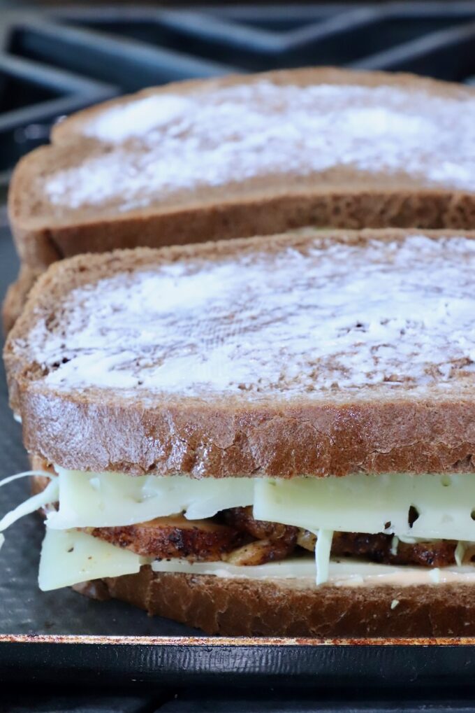 Two sandwiches on a stove. The bread is buttered, with melted cheese and grilled meat peeking out.