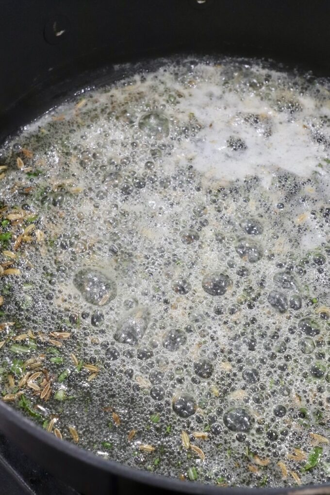 Close-up of seeds and herbs simmering in a bubbling, frothy liquid in a black pot
