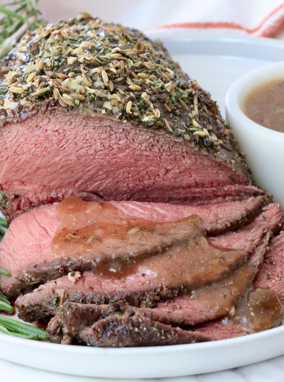Herb-crusted roast beef, thinly sliced and served on a white plate with brown gravy drizzled over the slices of beef.