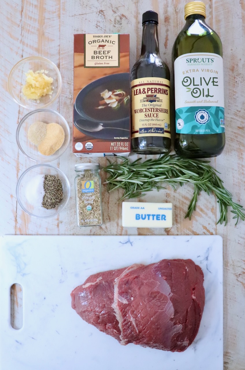 Ingredients for cooking a roast, including raw meat on a cutting board, a rosemary sprig, beef broth, olive oil, Worcestershire sauce, spices, and butter.