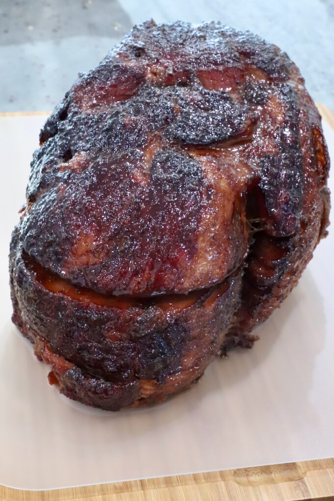 Close-up of a glazed, roasted ham on a wooden board. The ham's exterior is caramelized and crispy