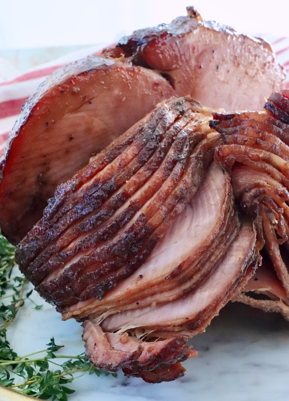 Sliced, glazed ham on a white platter with fresh thyme