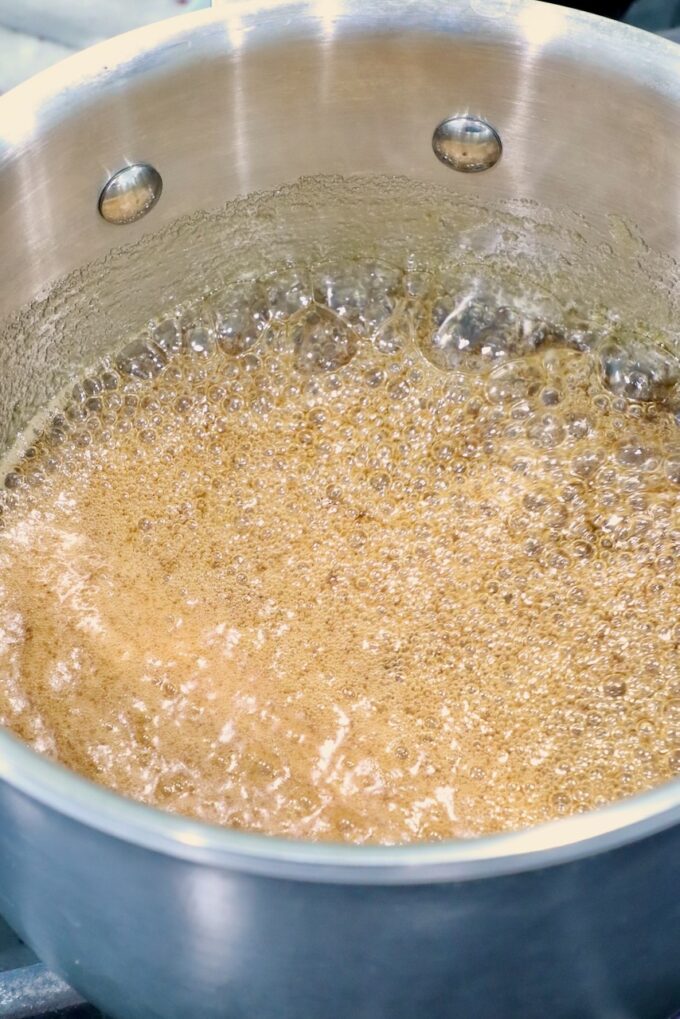 Ham glaze bubbling in a silver pot, creating an amber, frothy liquid. 
